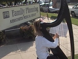 Girl playing harp in front of Family Planning Associates killing center